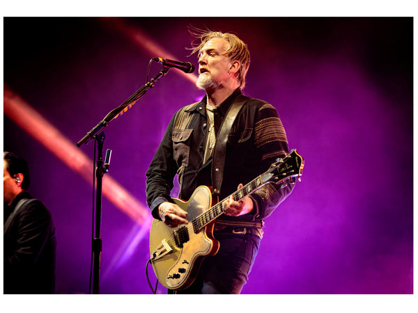Josh Homme is singing and playing guitar onstage at Glastonbury Festival 2023 with Queens of the Stone Age. Photography card by Tina K Photography