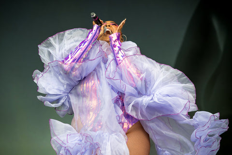 Lizzo on stage at Glastonbury, 2019 in a metallic purple bodysuit and sheer scarf