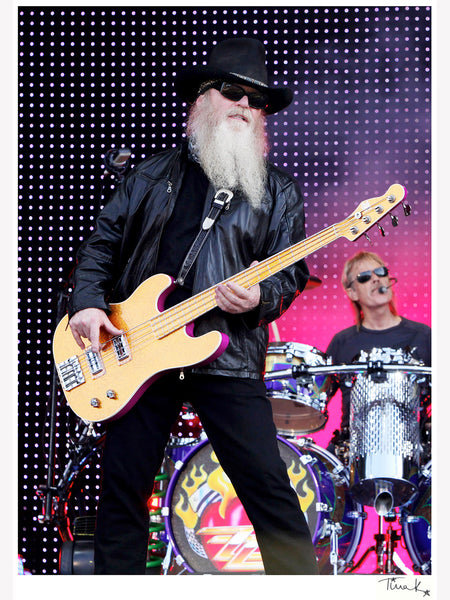 Dusty Hill of ZZ Top with bass guitar and black hat on stage at Download Festival 2009, Frank Beard drumming in background. Original print, signed by Tina K Photography.